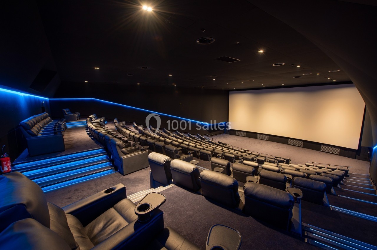 Salle de cinéma moderne avec sièges inclinables en cuir, éclairage tamisé et grand écran blanc.