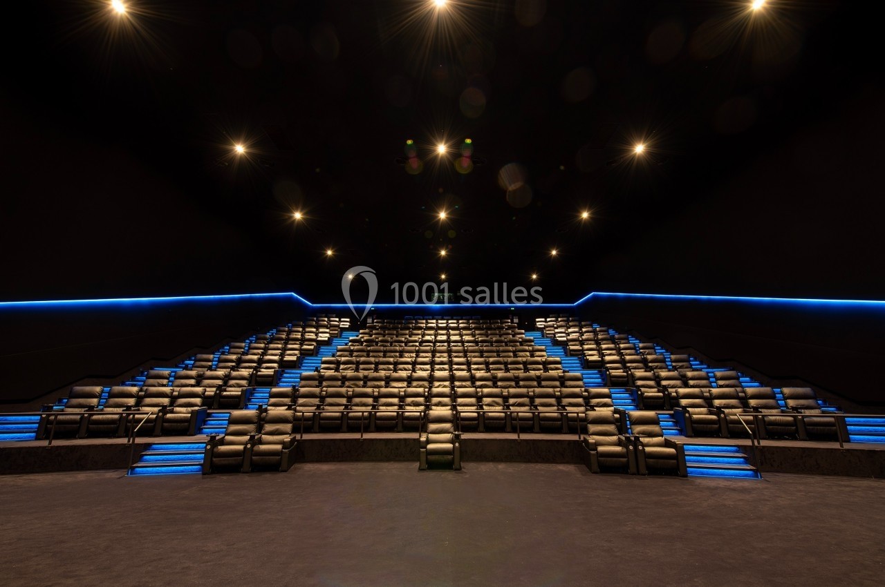 Salle de cinéma vide avec des rangées de sièges inclinables et des éclairages bleus sur les marches.