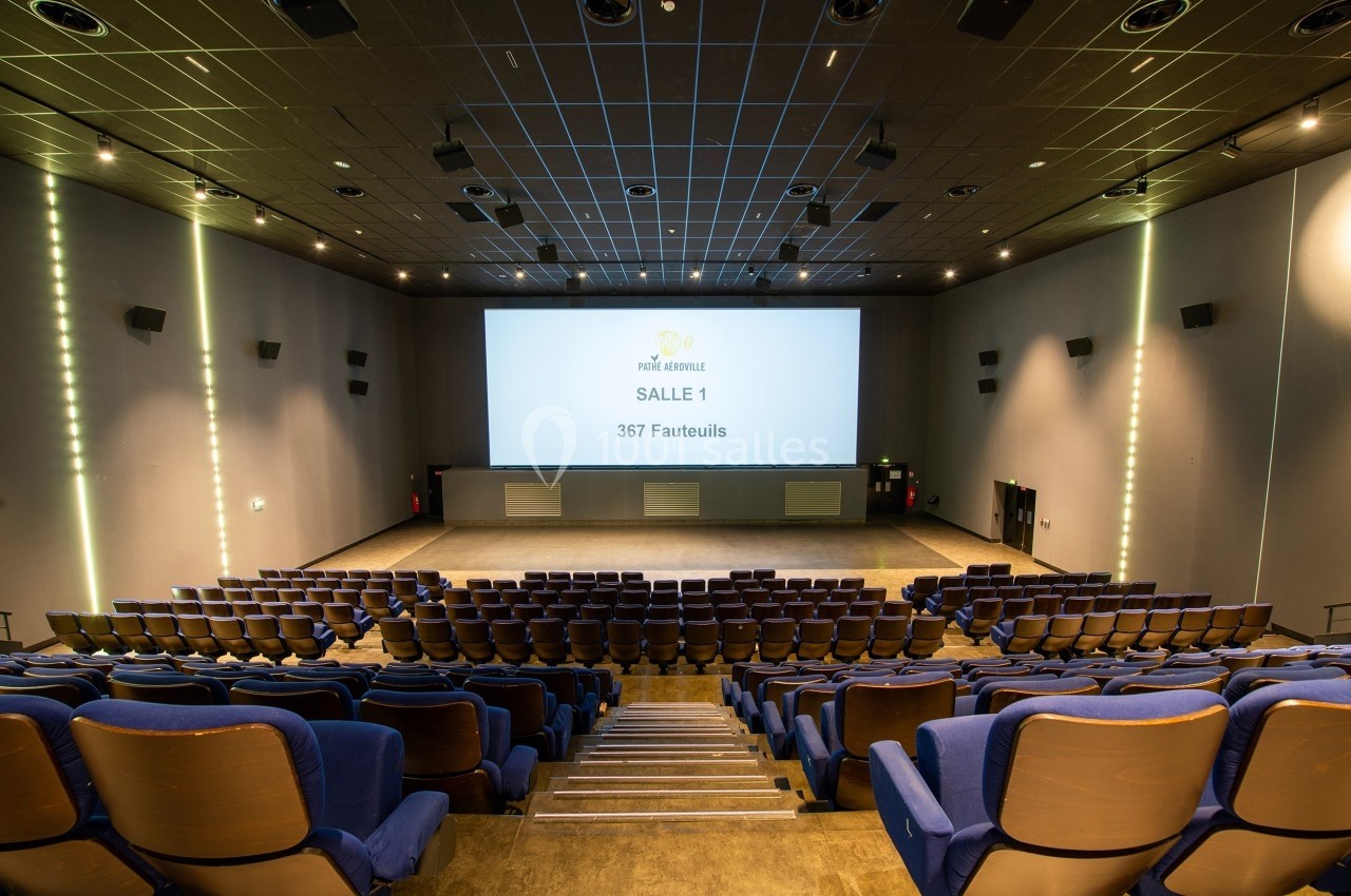 Salle de cinéma vide avec rangées de fauteuils bleus, écran géant allumé et éclairage tamisé.