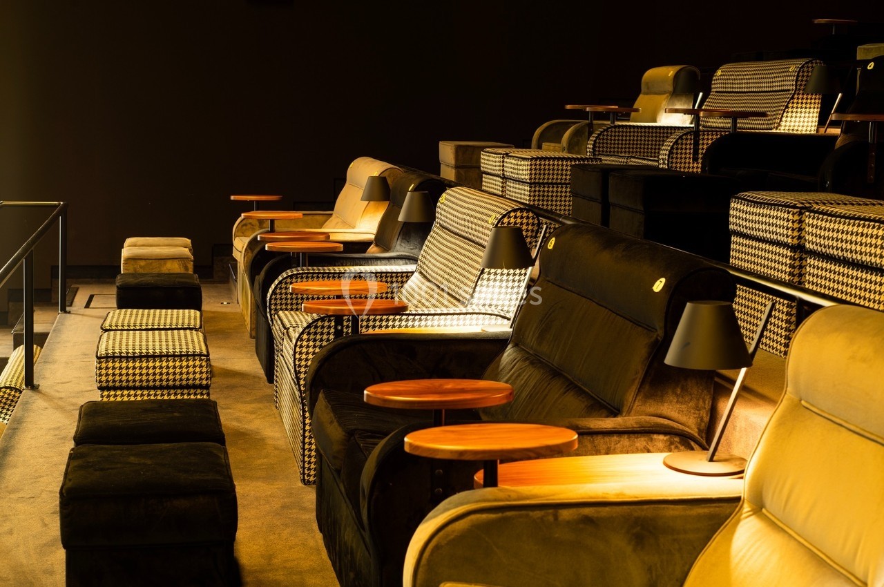 Fauteuils confortables avec lampes et tables en bois dans une salle de cinéma sombre.