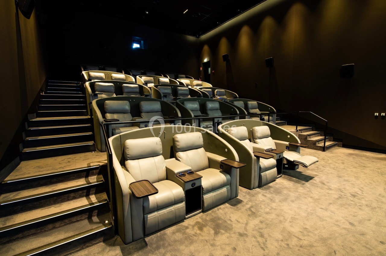 Salle de cinéma moderne avec fauteuils inclinables en cuir beige, accoudoirs équipés de porte-gobelets.