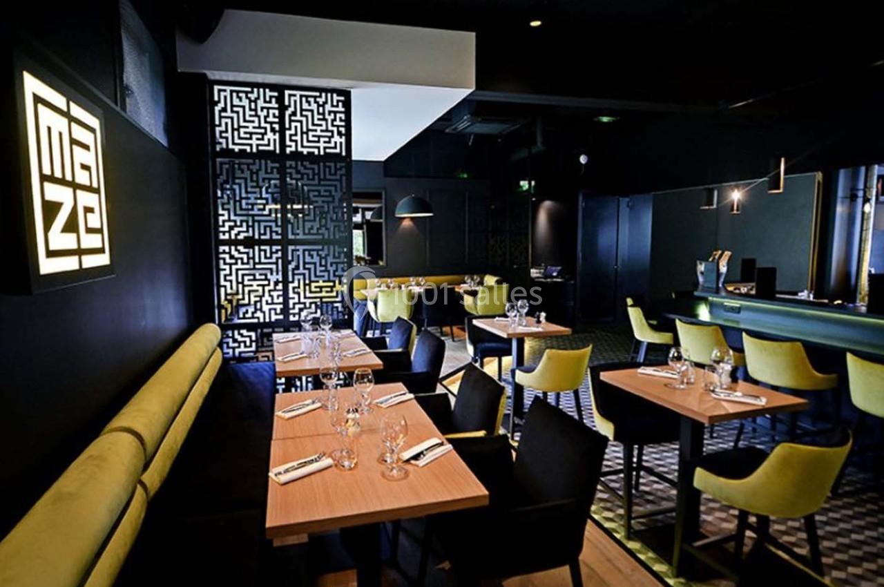 Salle de restaurant moderne avec tables en bois, chaises jaunes, banquettes vertes et éclairage tamisé.