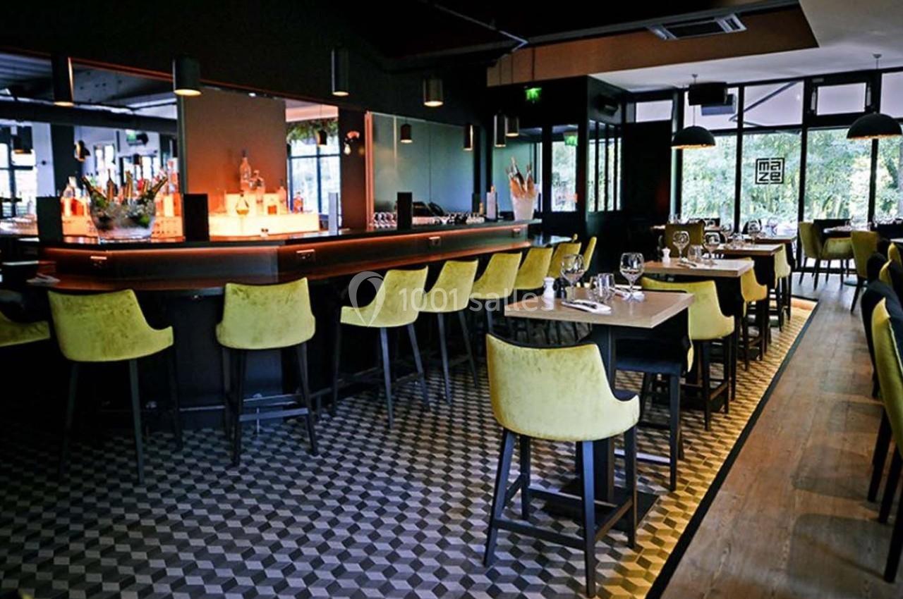 Intérieur d'un restaurant moderne avec un bar éclairé, des chaises jaunes et des tables dressées.