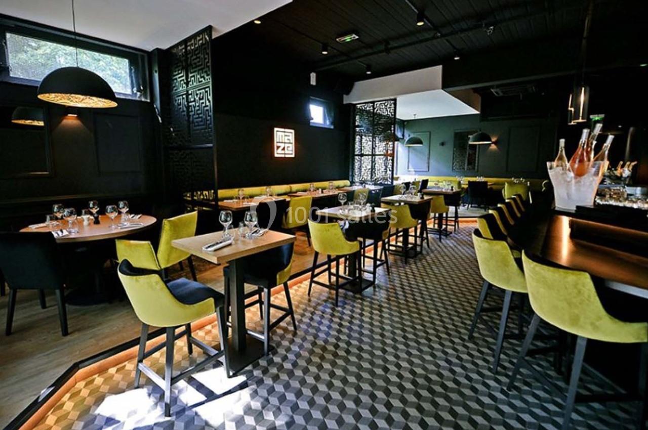 Salle de restaurant moderne avec tables dressées, chaises jaunes et noires, éclairage tamisé et sol à motifs géométriques.