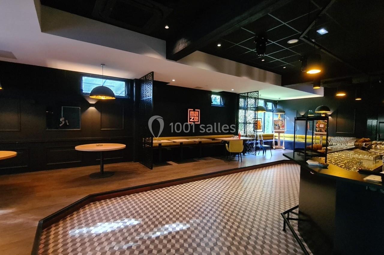 Salle de restaurant moderne avec tables, banquettes, bar et éclairage tamisé dans une ambiance sombre et élégante.