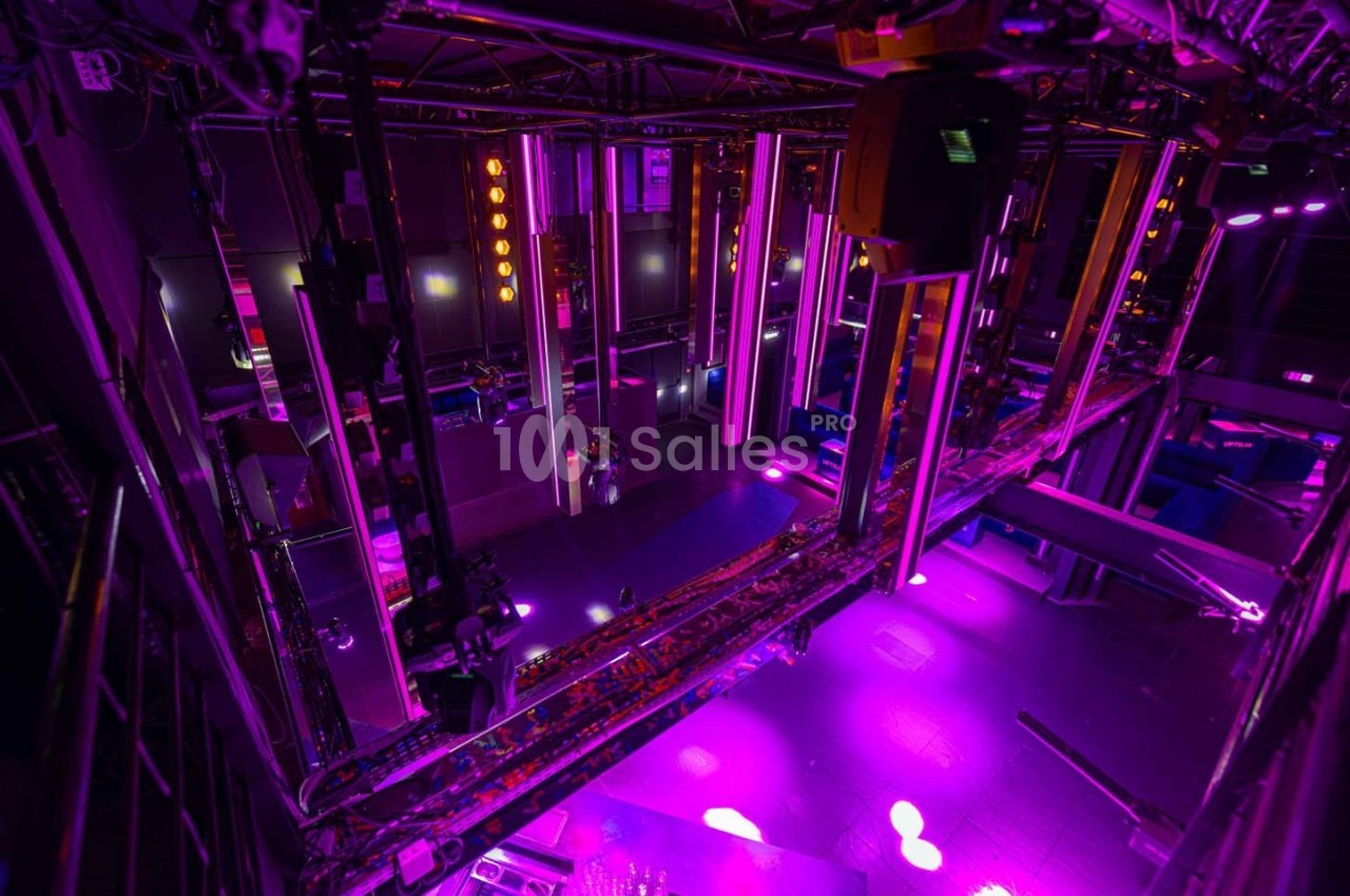 Vue plongeante d'une scène de théâtre ou de concert avec des éclairages violets et une structure technique suspendue.
