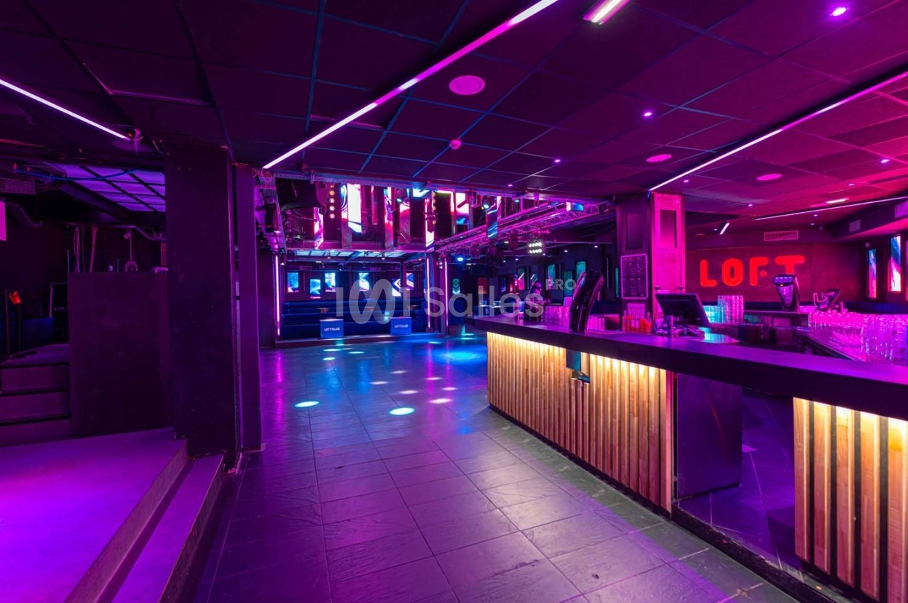 Intérieur d'une discothèque avec piste de danse éclairée par des lumières colorées et un bar en bois à droite.