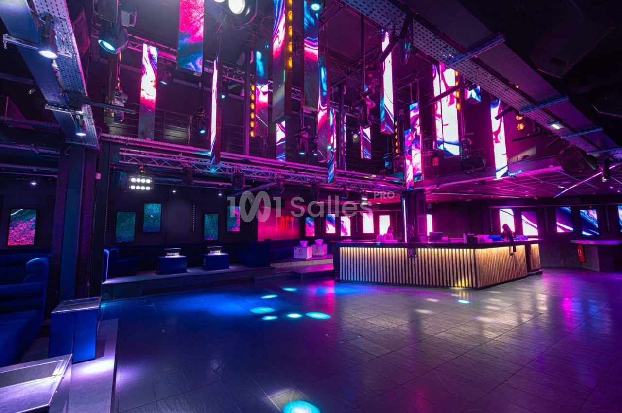 Salle de discothèque moderne avec éclairage coloré, piste de danse vide et comptoir lumineux en bois.