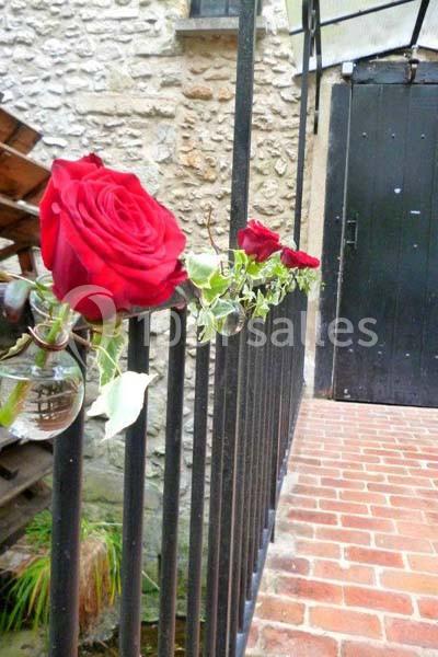 Roses rouges suspendues à une rambarde en métal devant une porte noire et un mur en pierre.