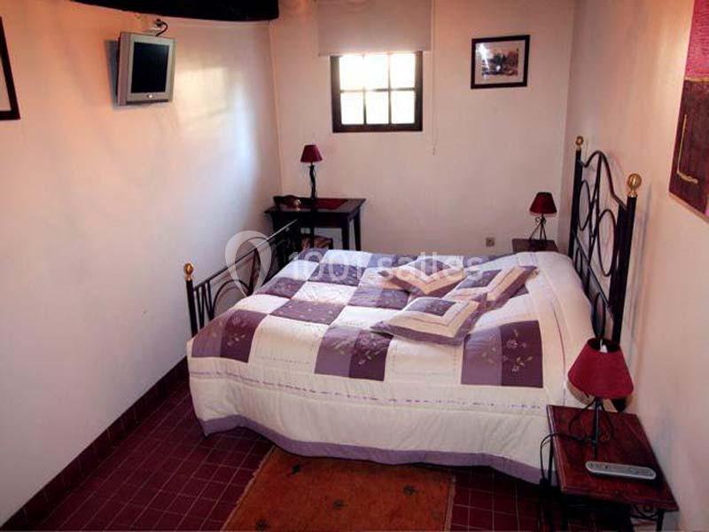 Chambre avec lit double, couvre-lit à motifs violets, deux lampes de chevet et une petite fenêtre.