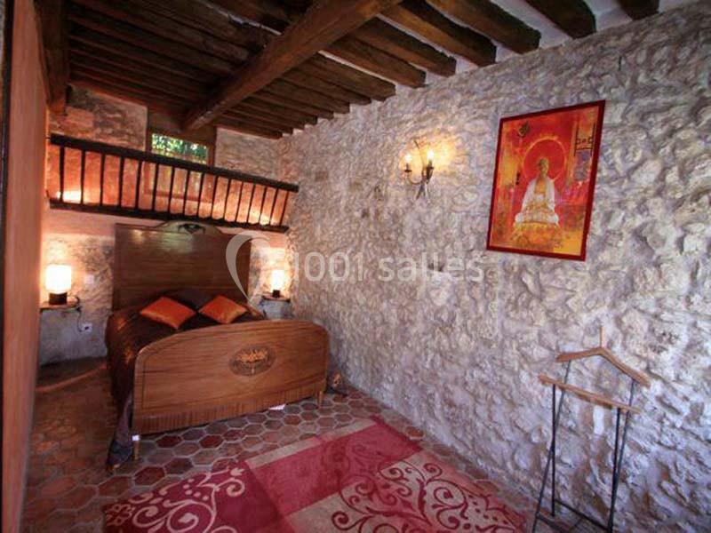 Chambre rustique avec murs en pierre, lit en bois, poutres apparentes et décoration murale colorée.