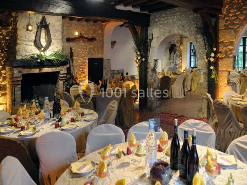 Salle de réception rustique avec murs en pierre, tables décorées et chaises couvertes, éclairage chaleureux.