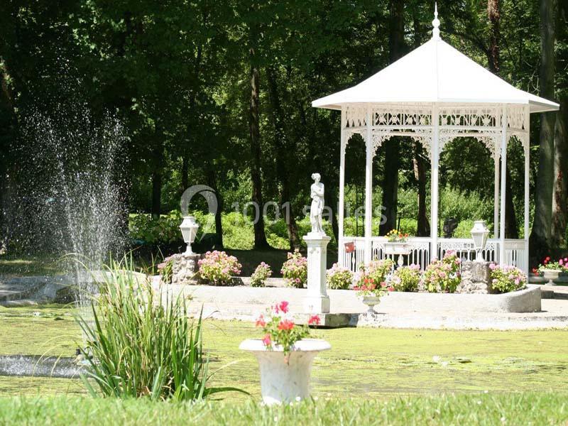 Kiosque blanc entouré de fleurs près d'un bassin avec une fontaine, dans un parc verdoyant.