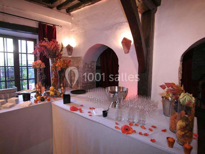 Table décorée pour un événement, avec verres alignés, fleurs colorées et éléments automnaux dans une salle rustique.