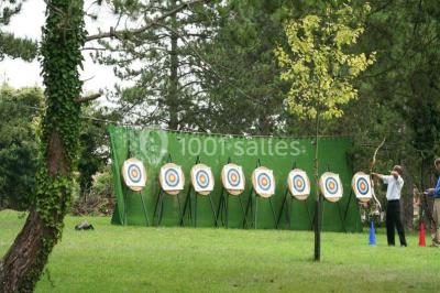 Miniature Location salle Messy (Seine-et-Marne) - Moulin de Moulignon #22 Cibles de tir à l'arc alignées sur un terrain herbeux, entourées d'arbres, avec deux personnes à proximité.