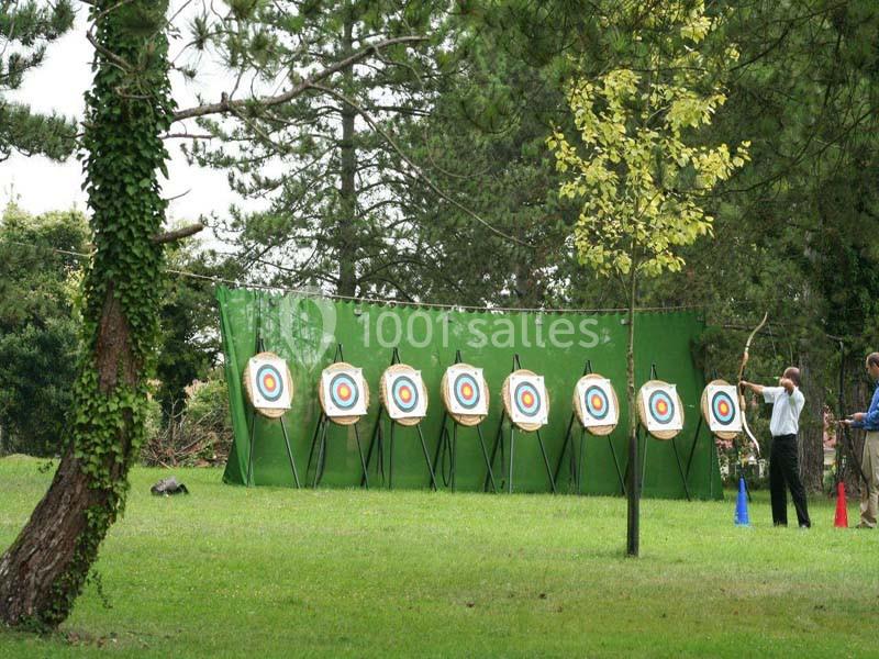 Cibles de tir à l'arc alignées sur un terrain herbeux, entourées d'arbres, avec deux personnes à proximité.