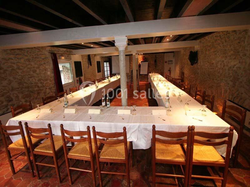 Salle de réunion avec tables disposées en U, chaises en bois, murs en pierre et plafond avec poutres apparentes.