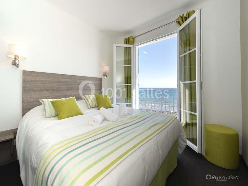 Chambre lumineuse avec lit double, décorée en vert et blanc, donnant sur un balcon avec vue sur la mer.