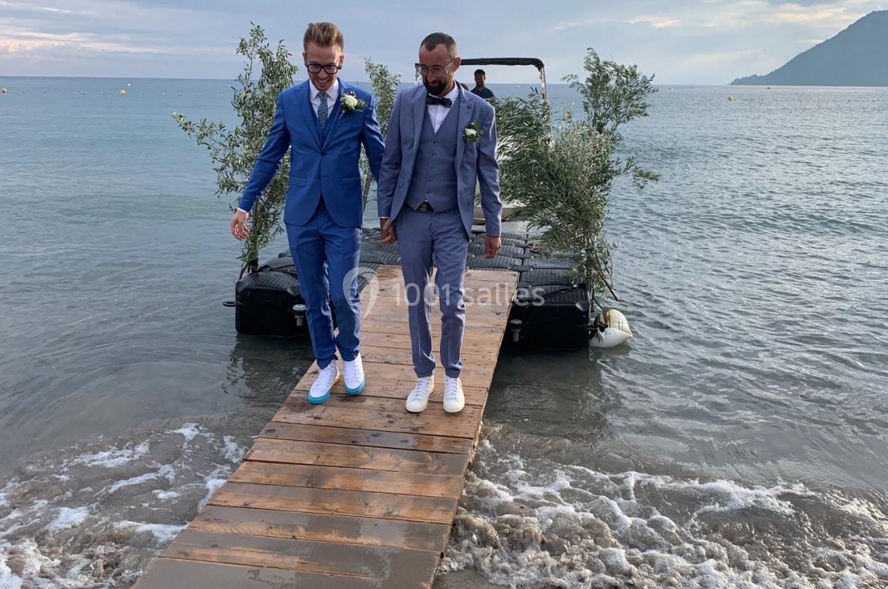 Deux hommes en costume marchant main dans la main sur un ponton en bois au bord de la mer.