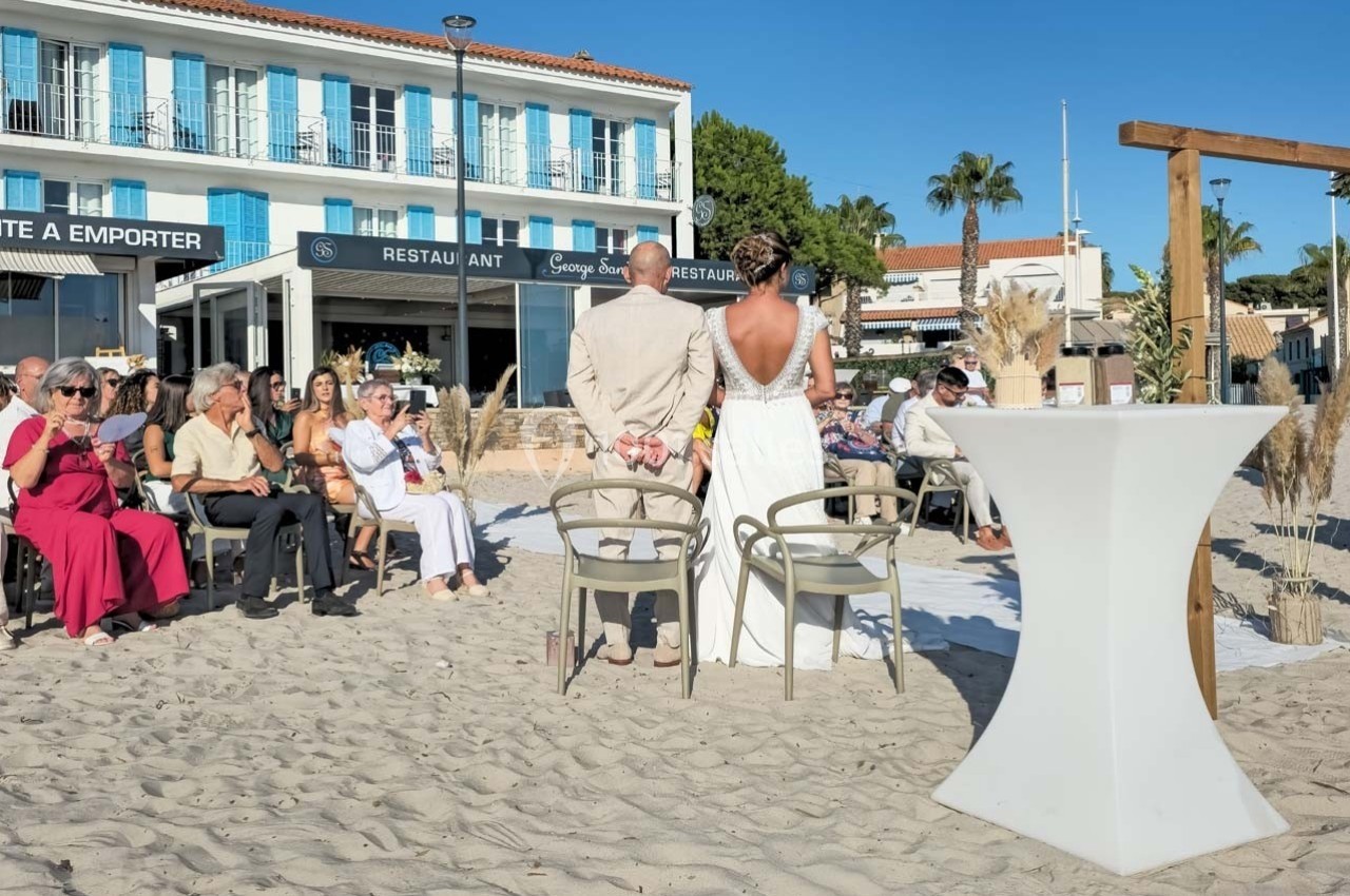 Cérémonie de mariage en extérieur sur une plage, avec des invités assis et un couple debout face à l'autel.