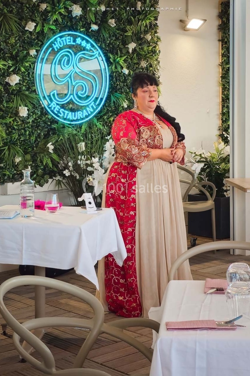 Une femme en robe traditionnelle se tient debout dans un restaurant décoré de plantes et d'un néon lumineux.