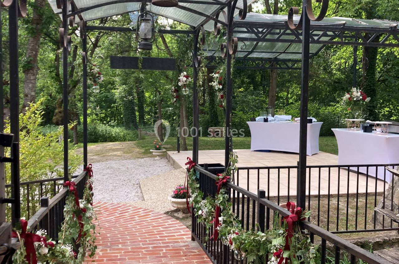 Passage en brique couvert de fer forgé décoré de fleurs, menant à une terrasse aménagée pour un événement en plein air.