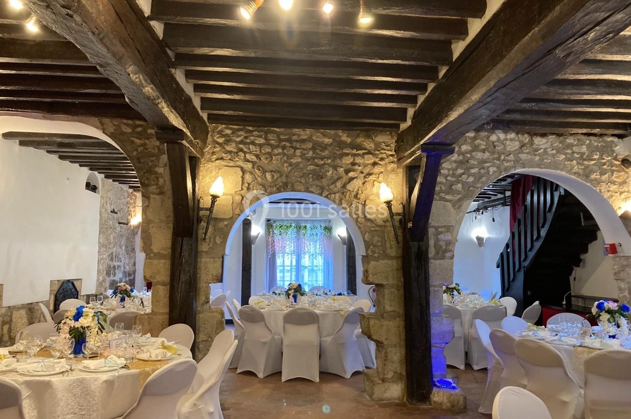 Salle de réception avec murs en pierre, poutres apparentes et tables décorées pour un événement.