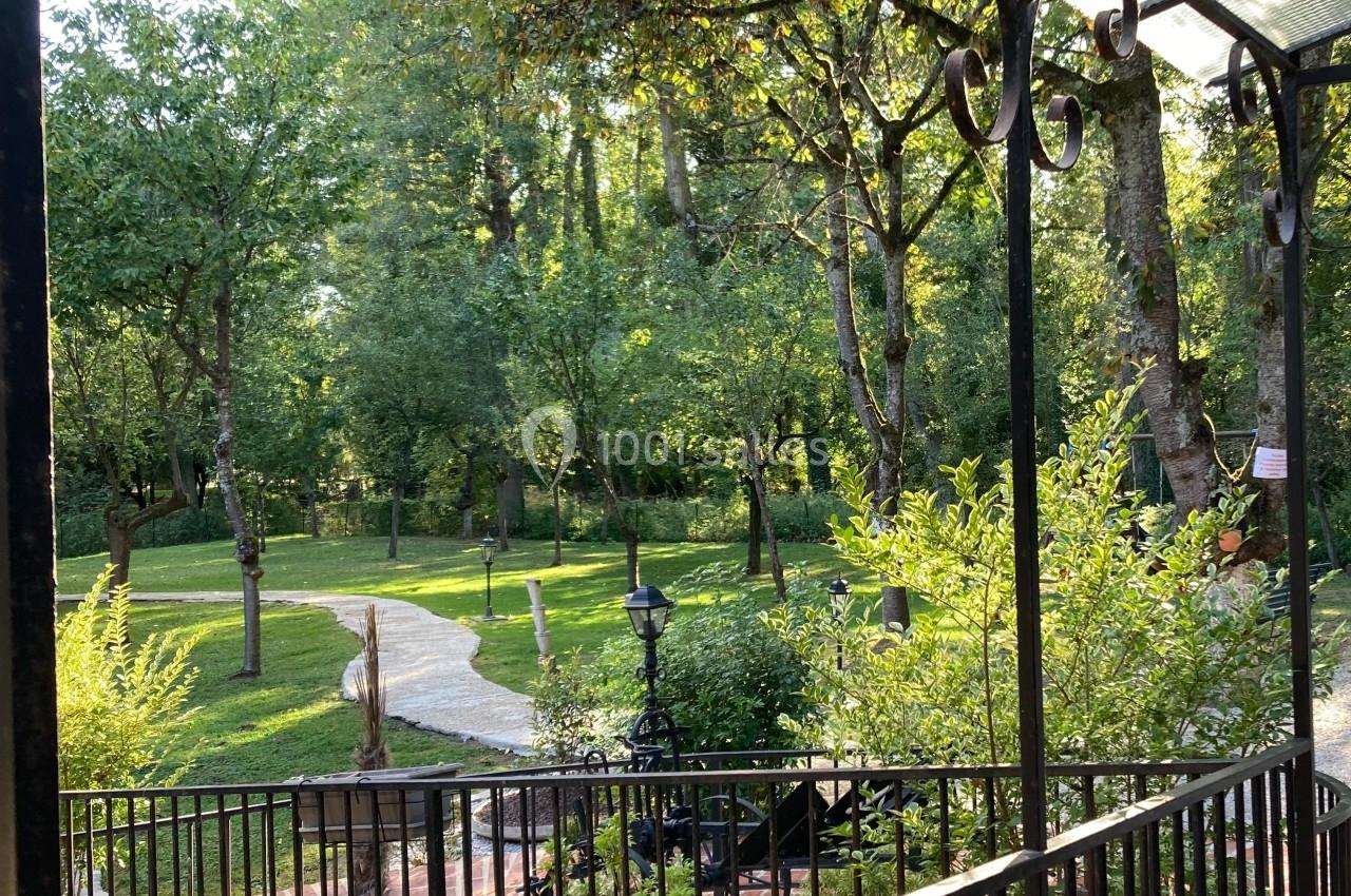Vue sur un jardin verdoyant avec des arbres, un chemin sinueux et une balustrade en premier plan.