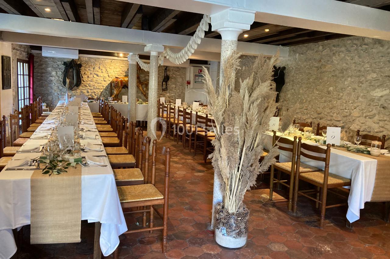 Salle de réception avec tables alignées, nappes blanches, décorations végétales et murs en pierre apparente.