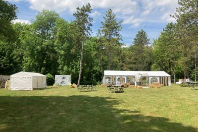 Tentes blanches installées sur une pelouse entourée d'arbres, avec tables et bottes de foin disposées en extérieur.