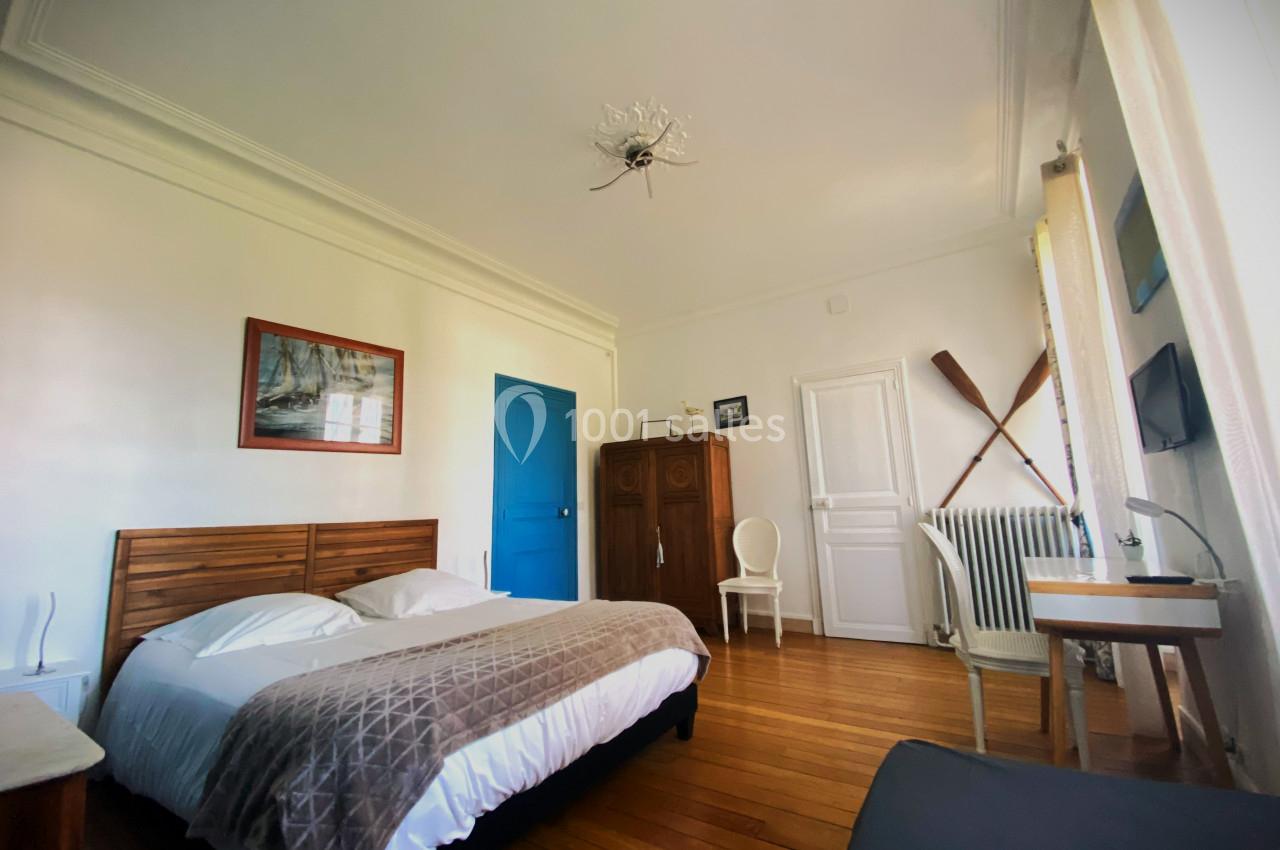 Chambre lumineuse avec lit double, parquet en bois, armoire, décoration murale et fenêtre avec rideaux clairs.