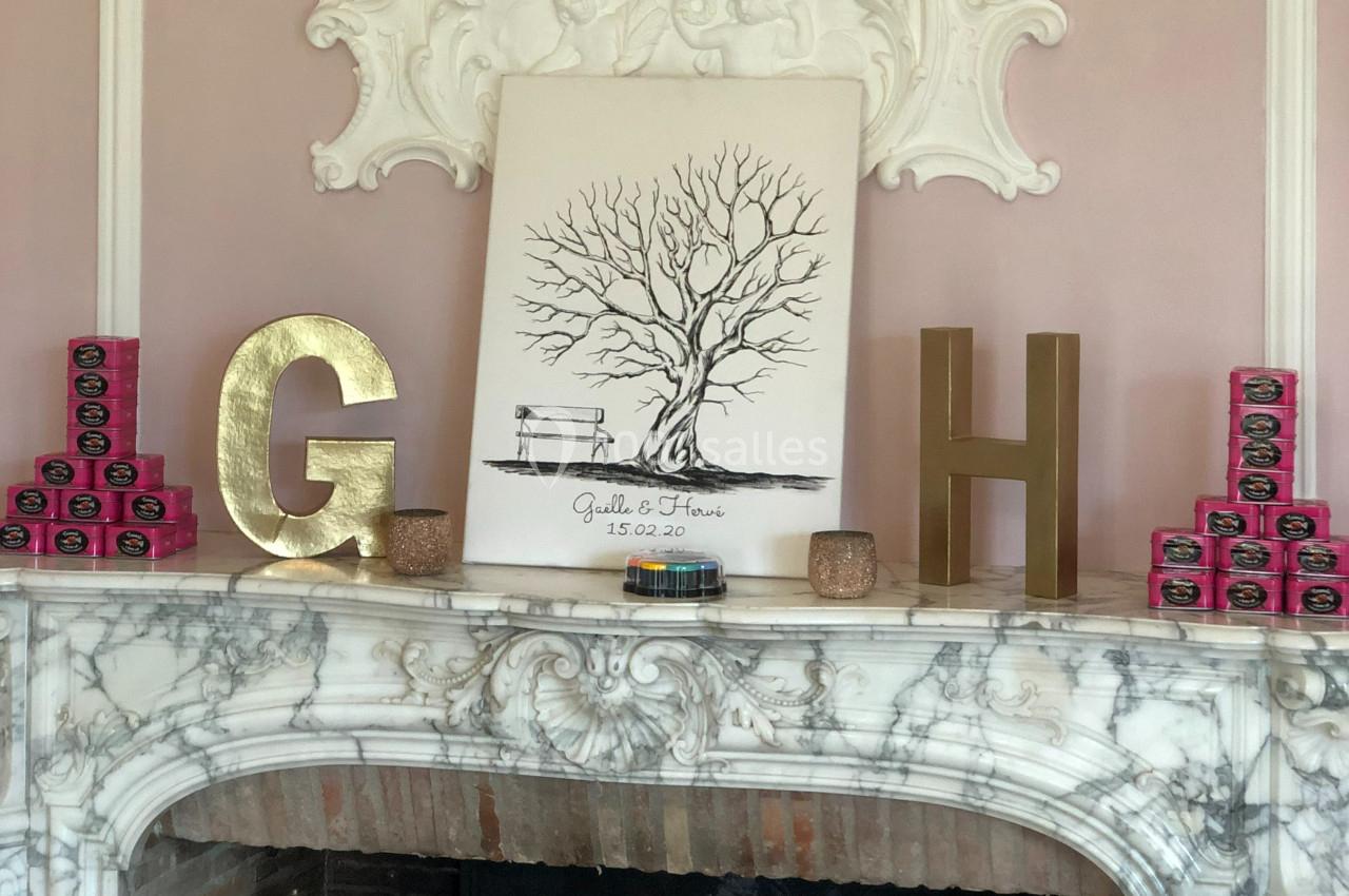 Tableau d'arbre nu avec banc et prénoms, posé sur une cheminée en marbre, entouré de décorations dorées et roses.