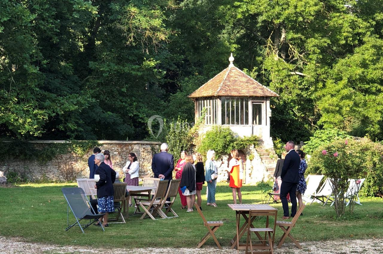 Groupe de personnes discutant dans un jardin avec des tables en bois, près d'une petite rotonde entourée de verdure.