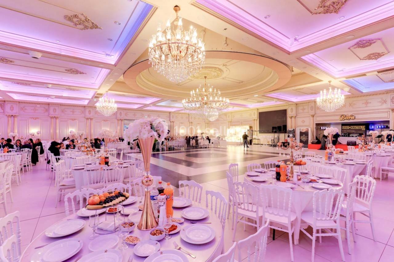 Salle de réception élégante avec tables dressées, chandeliers imposants et éclairage rose tamisé.