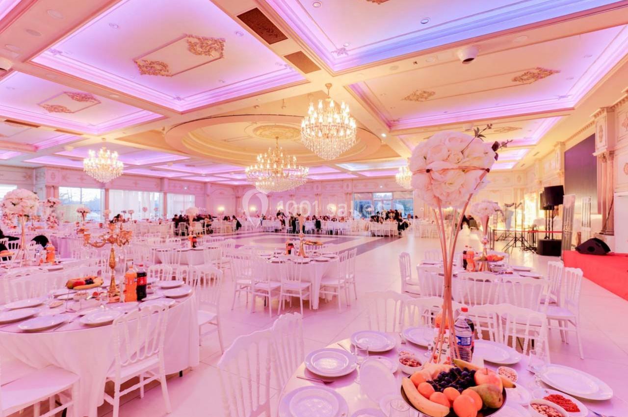 Salle de réception élégante avec tables dressées, décorations florales et éclairage rose sous des lustres imposants.
