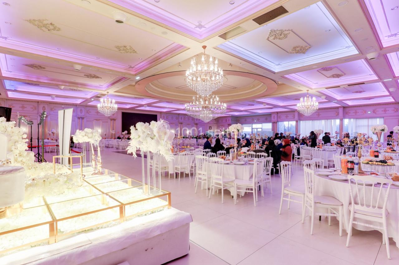 Salle de réception élégante avec tables décorées, lustres imposants et éclairage rose tamisé.