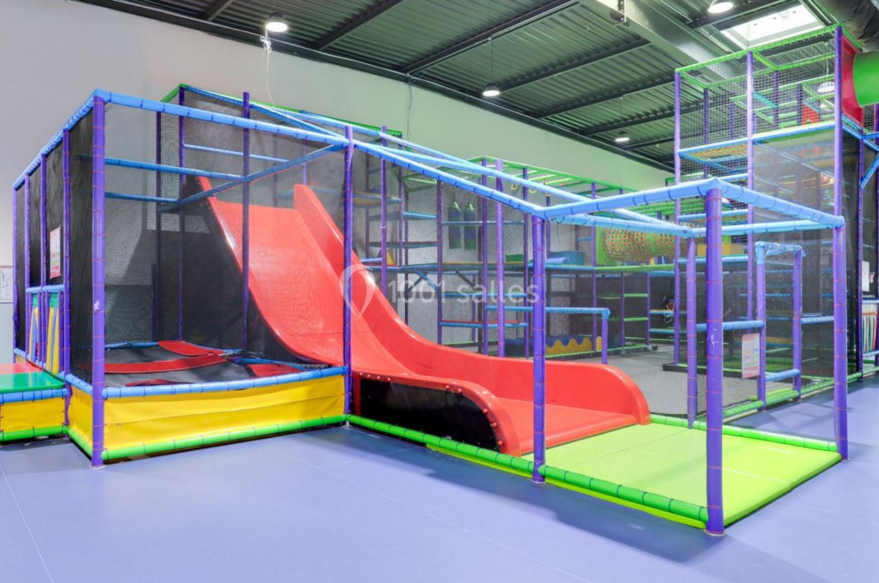 Structure de jeu intérieure avec toboggans rouges, tunnels et filets, conçue pour les enfants dans un espace couvert.