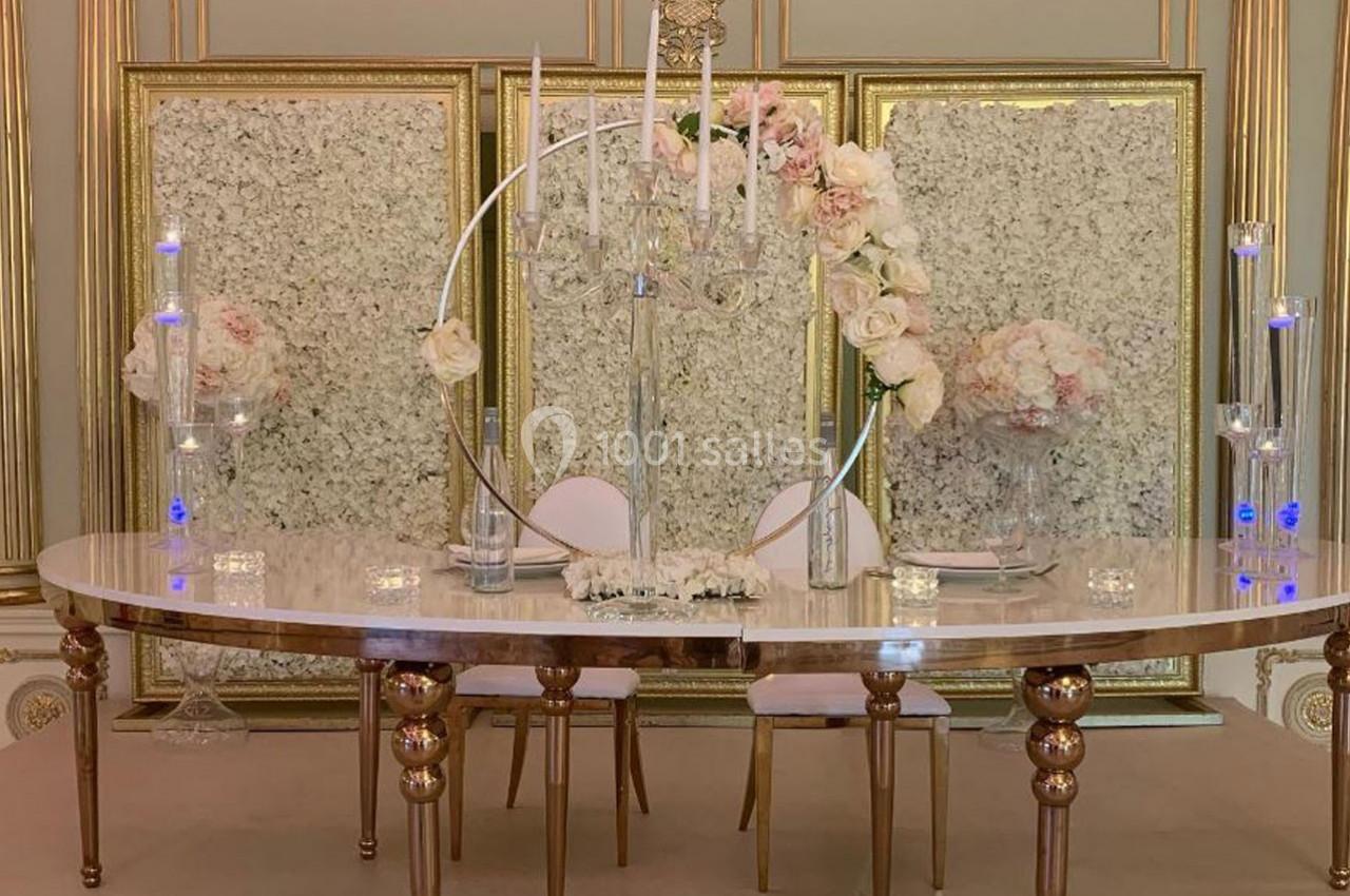 Table décorée avec des chandeliers, des fleurs blanches et roses, devant des panneaux ornés de motifs floraux.