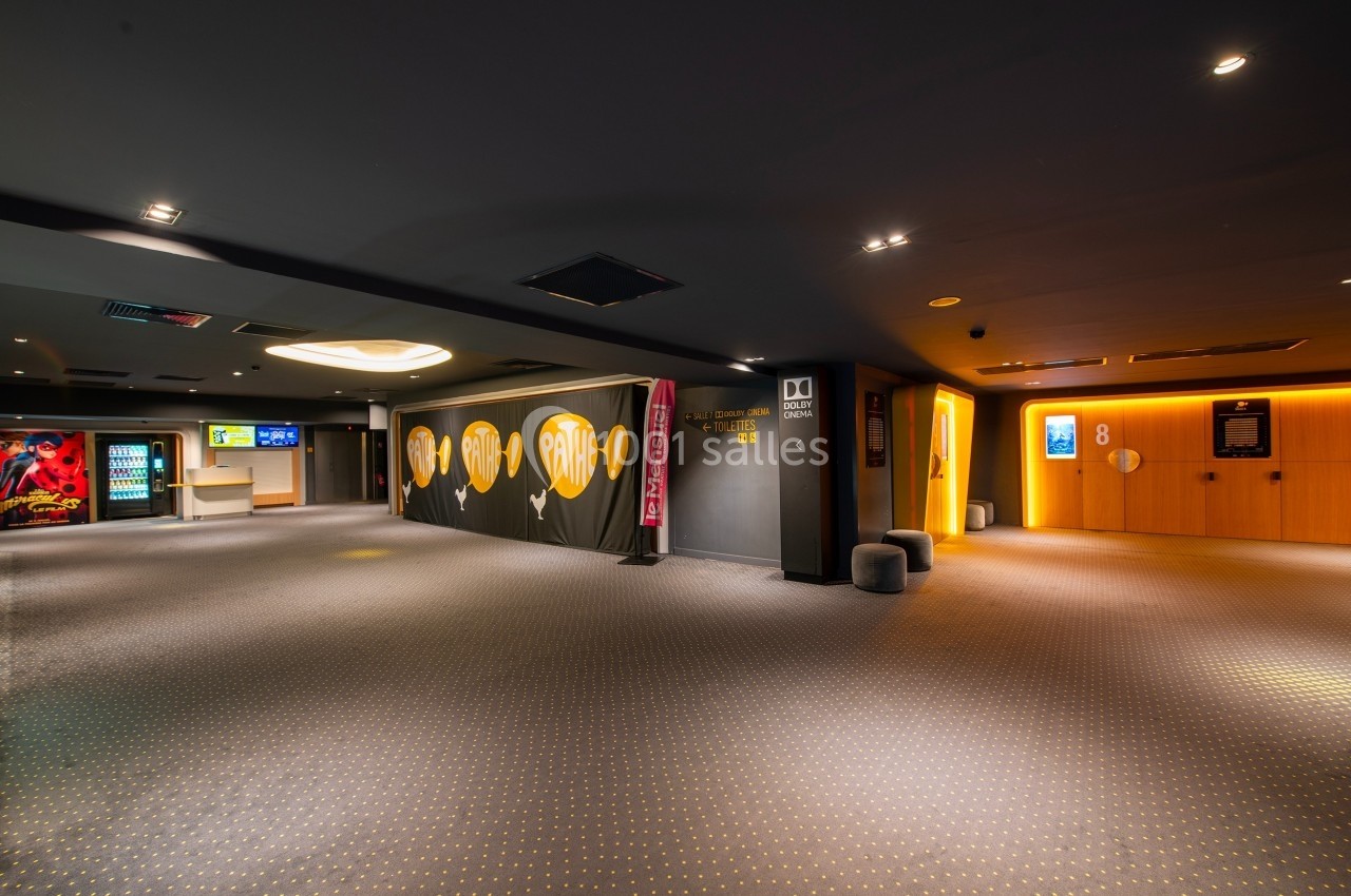 Hall d'entrée d'un cinéma avec moquette, affiches lumineuses, distributeurs automatiques et accès aux salles numérotées.
