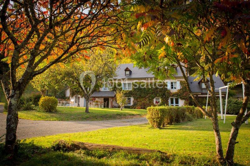 Maison en pierre recouverte de lierre, entourée d'arbres aux feuilles automnales et d'un jardin verdoyant.