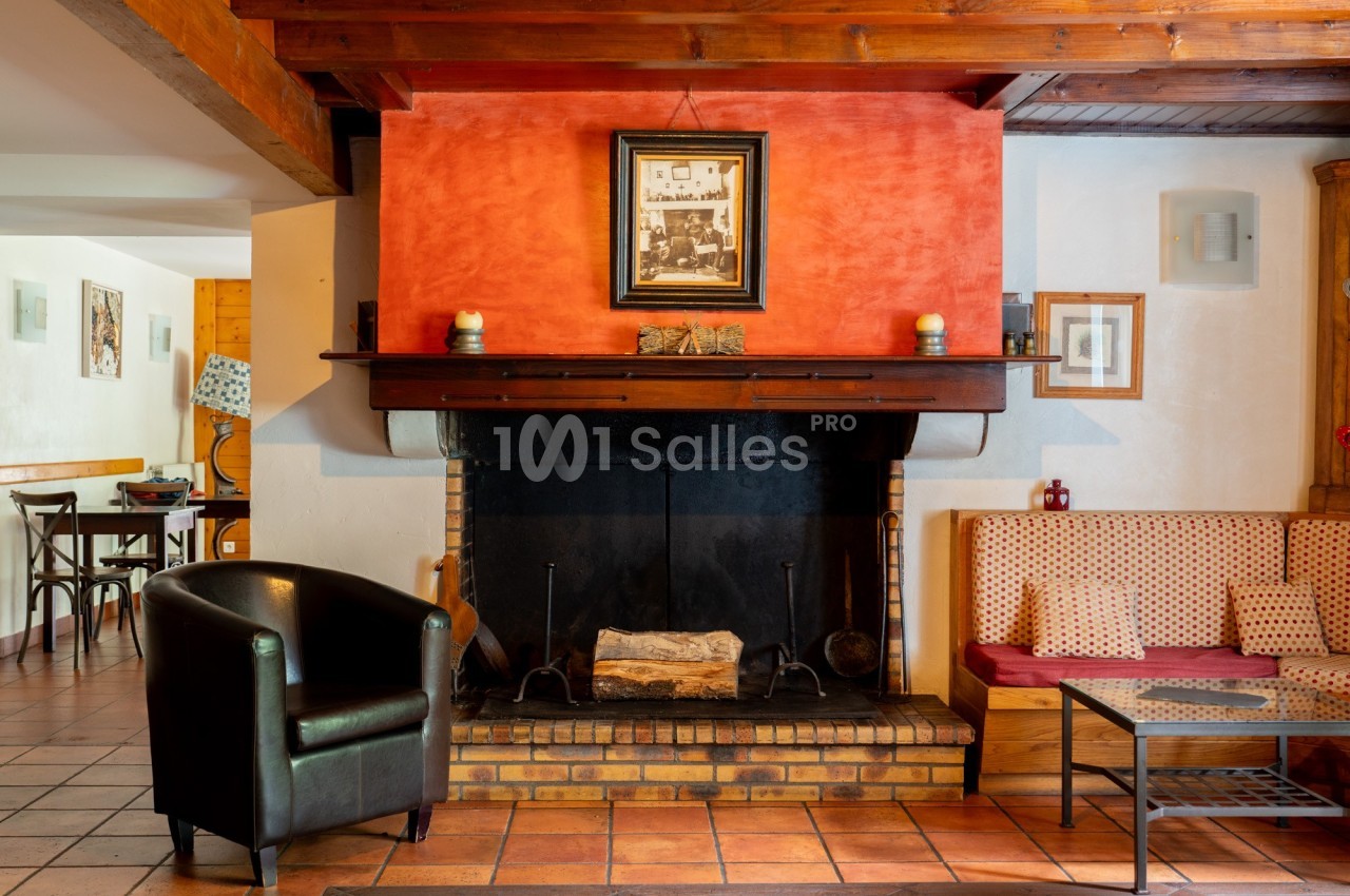 Cheminée en briques noires avec un cadre au-dessus, entourée de fauteuils et d'un canapé dans une pièce chaleureuse.