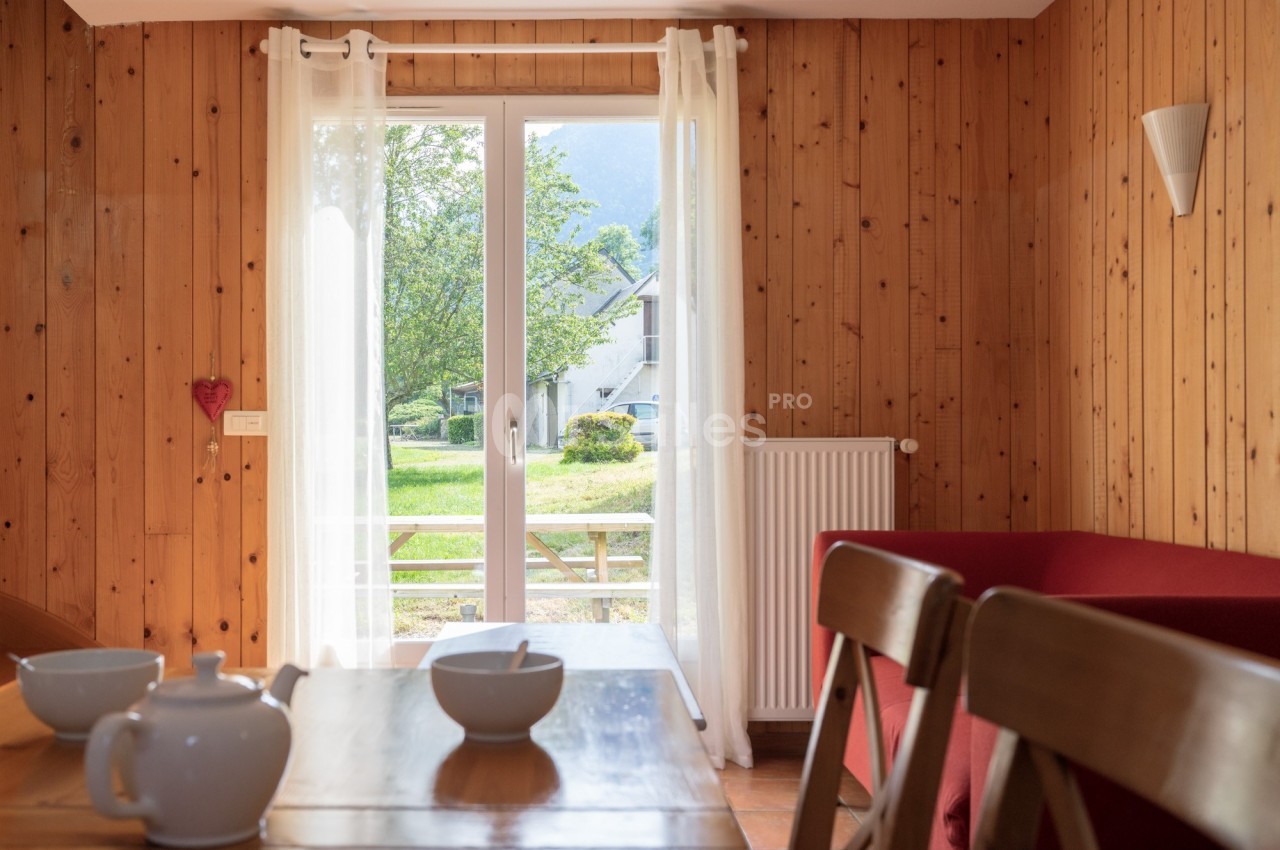 Porte-fenêtre donnant sur un jardin verdoyant, vue depuis une salle à manger avec table en bois et chaises.