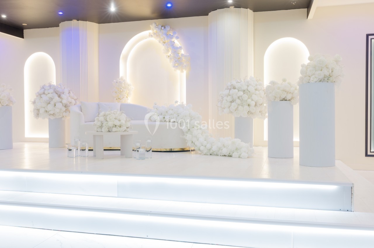 Décor élégant avec canapé blanc, colonnes et arrangements floraux blancs dans un espace lumineux et moderne.