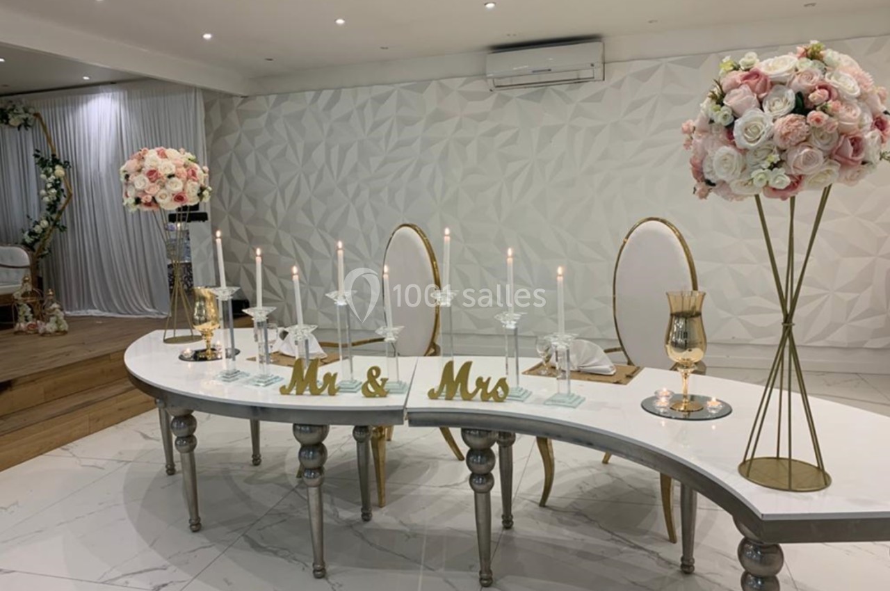 Table décorée pour un mariage avec chandeliers, fleurs roses et blanches, et inscriptions ’Mr & Mrs’ dorées.