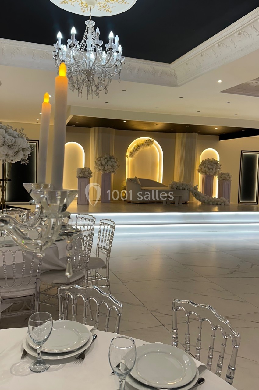 Salle de réception élégante avec table dressée au premier plan et scène décorée de fleurs en arrière-plan.