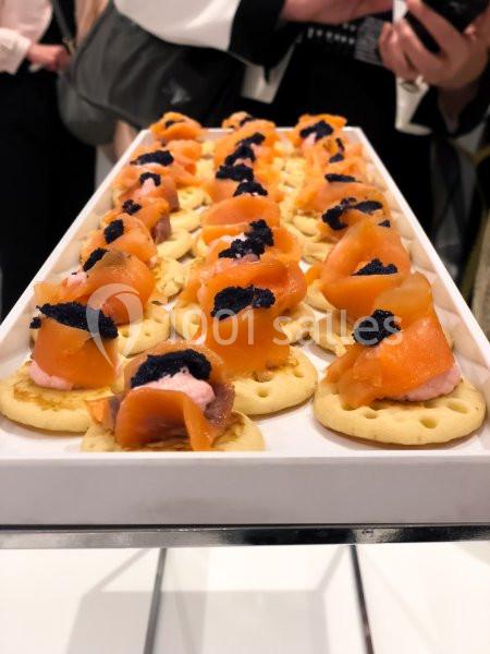 Plateau de canapés garnis de saumon fumé, crème rose et œufs de poisson noir, disposés sur des biscuits salés.