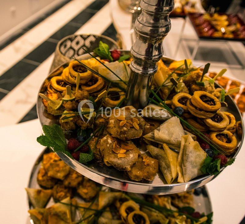 Plateau de pâtisseries et amuse-bouches variés disposés sur deux étages, décoré de feuilles de menthe et fruits rouges.
