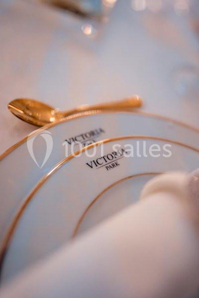 Assiette blanche bordée d'or avec l'inscription ’Victoria Park’, accompagnée d'une cuillère dorée.