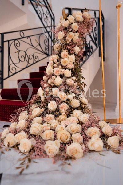 Arrangement floral de roses blanches et roses tombant en cascade devant un escalier à rambarde en fer forgé.