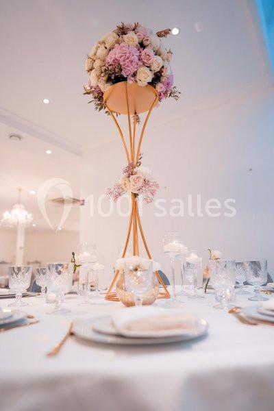 Centre de table élégant avec un bouquet de fleurs roses et blanches sur un support doré, entouré de vaisselle raffinée.